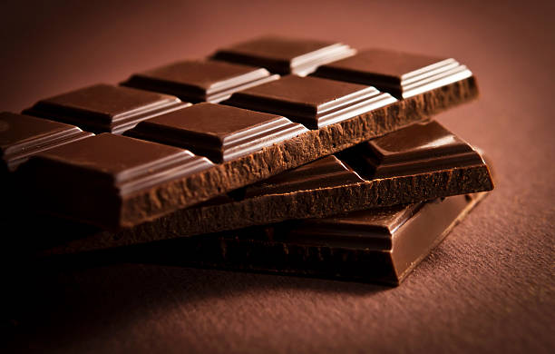 Dark chocolate bar cut in three pieces over brown surface