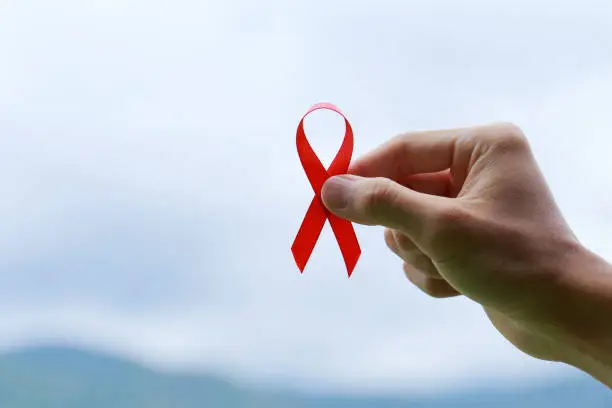Close up hands holding an aids red ribbon on nature background.healthcare and medicine concept