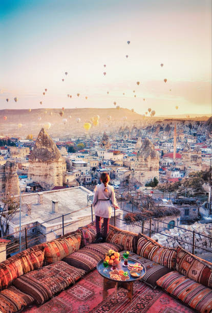 belle donne stanno sul tetto dell'hotel a guardare le mongolfiere che sorvolano la città di ürgüp cappadocia, in turchia - hot air balloon landscape sunrise mountain foto e immagini stock