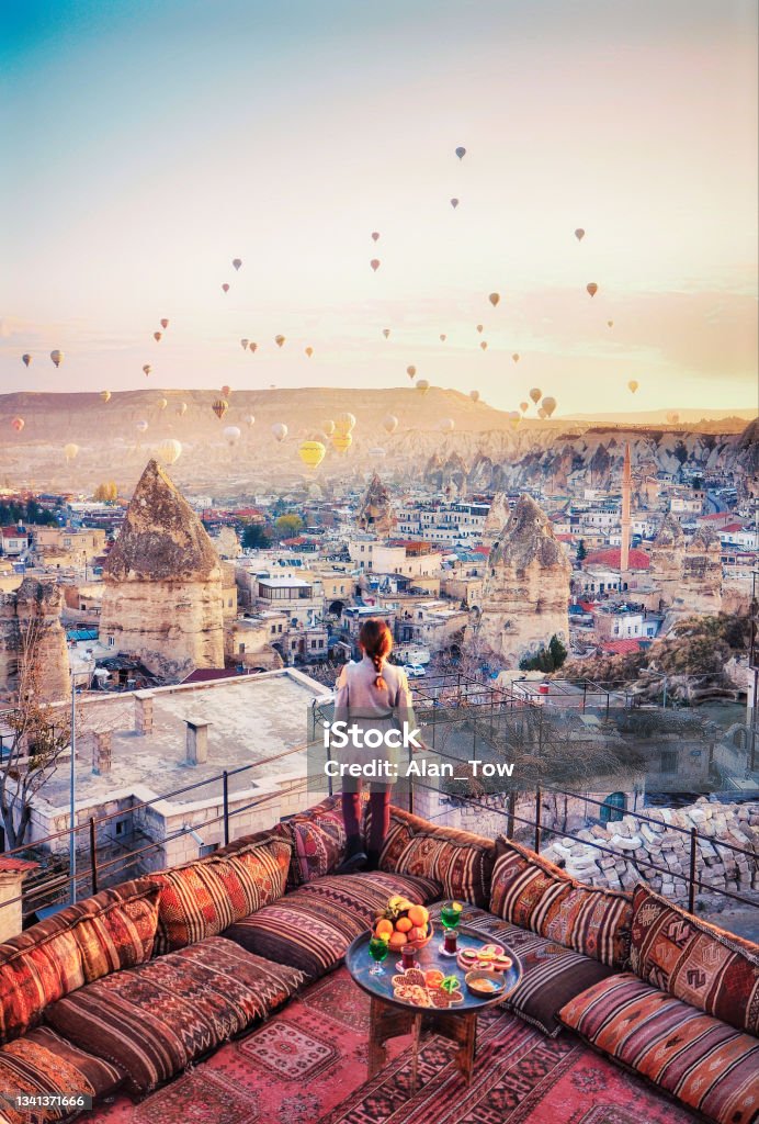 Beautiful women stand at hotel rooftop watching hot air balloons flying over city Ürgüp Cappadocia, Turkey Travel Stock Photo