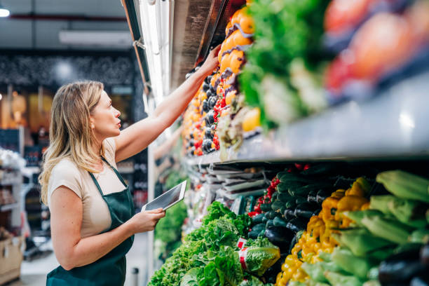 Female owner checking inventory at store Female owner working at supermarket. Saleswoman is taking inventory in store. She is wearing apron. saleswoman stock pictures, royalty-free photos & images