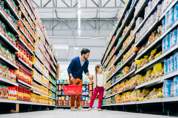 Daughter buying groceries with father in store Father and daughter shopping in store. Girl is picking food product in supermarket. They are in casuals. holding shopping basket stock pictures, royalty-free photos & images