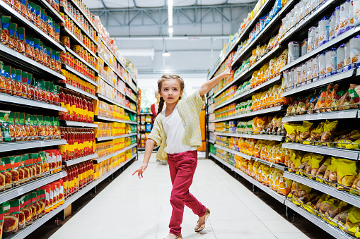 Carefree girl running in grocery store. Cheerful female child is at aisle in supermarket. She is having braided hair.