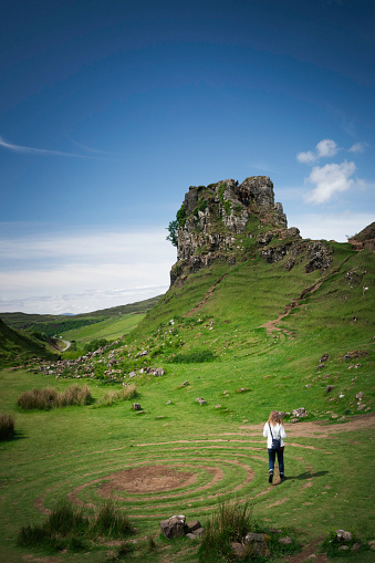 Blond tourist walks around the fairy circle at the green hills of Fairy Glen, Isle of Skye, Scotland, UK, Europe