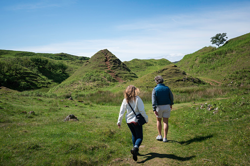 Wide angle shot of a group of mixed ethnic teens on a walk along the coastline together at Holy Island in the North East of England in summer. They are running up a hill, laughing together.