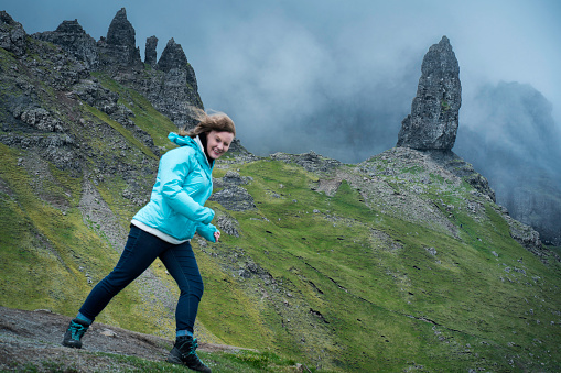 Teen girl braces herself against strong winds while hiking the Old Man of Storr on Isle of Skye, Scotland, UK, Europe