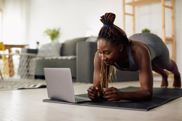 istock African American athlete using her laptop while exercising in plank position at home. 1341378780