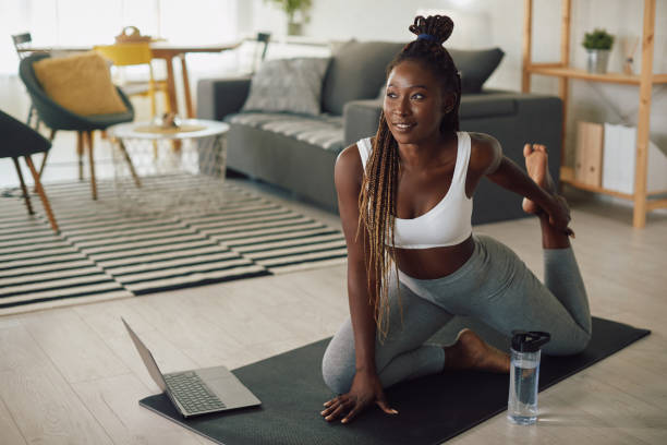 istock Young African American sportswoman stretching while warming up during online exercise class at home. 1341378808
