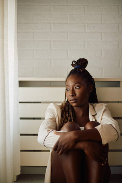Depressed black woman looking through the window while being alone at home.