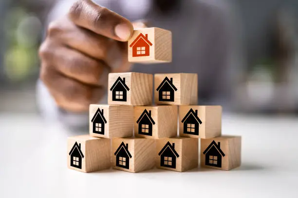 Real Estate House Community. African Man Stacking Housing Blocks