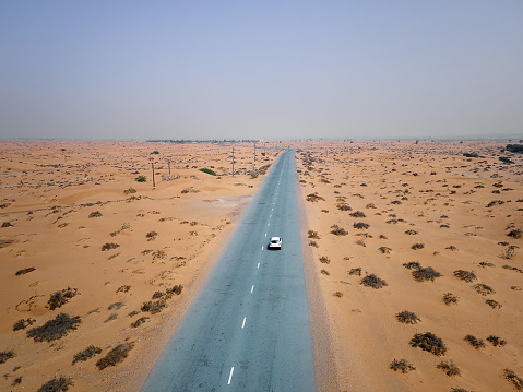 White car on a scenic desert road surrounded with sand dunes in the United Arab Emirates near Dubai aerial drone top view