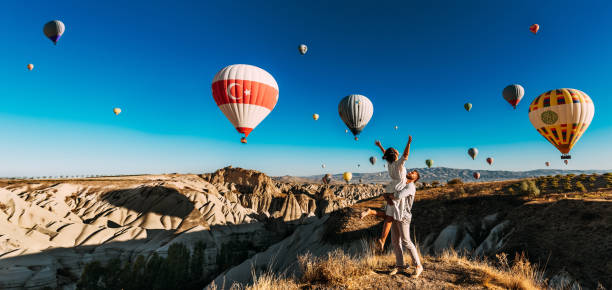 A happy couple among balloons in Cappadocia. A couple in love against the background of flying balloons in Cappadocia. Travel to Turkey. Balloons in the sky, panorama. Wedding trip. Honeymoon trip stock photo