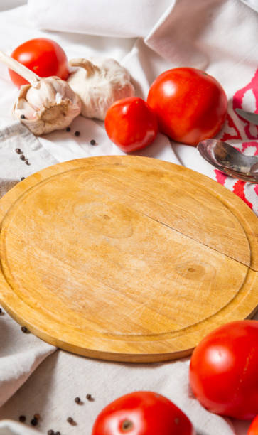 istock A table with different fabrics, on which lies a round board, around red ripe tomatoes and garlic. Vertical photo. 1341388168