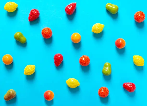 Photo of Bright chewy candies in the shape of fruits scattered on a blue background. Top view. Creative sweets background.