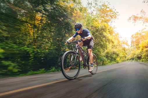 Cyclist in full gear going up a mountain road through forest. His friends way behind.