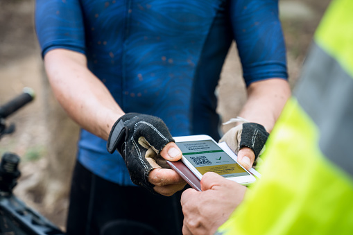 Selective focus, Mountain bike athlete show health passport of vaccination certification on phone at bicycle race track, to certify have been vaccinated of coronavirus. Sport during Covid-19 pandemic.
