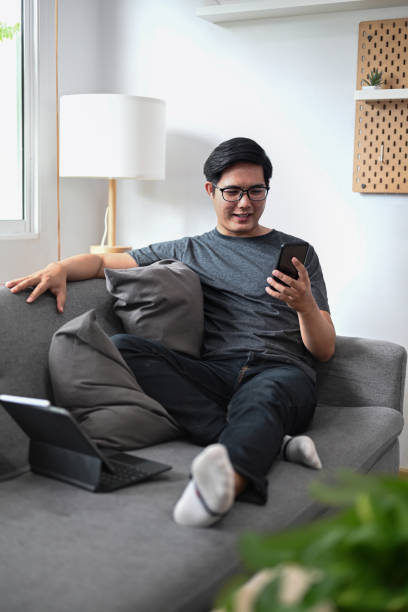 istock Young Asian man sitting on sofa and using smart phone. 1341394225