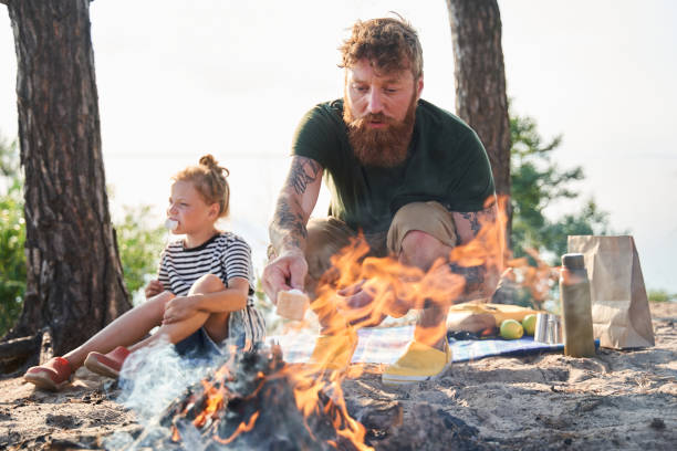 istock Man sitting on the knees near the campfire and preparing a fried marshmallows 1341394387