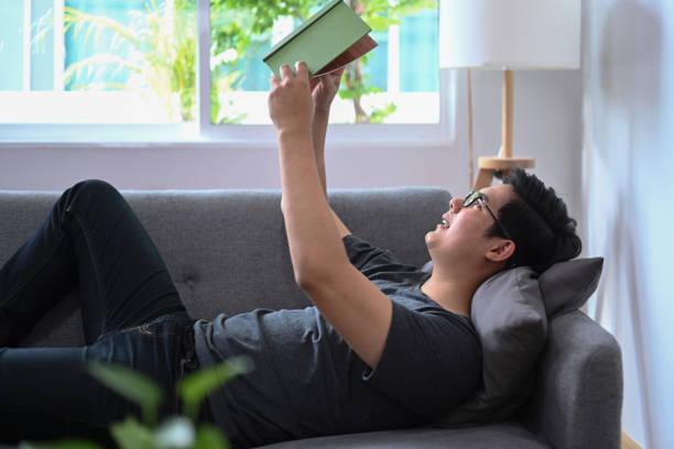istock Man lying on comfortable sofa in living room and reading a book. 1341394432