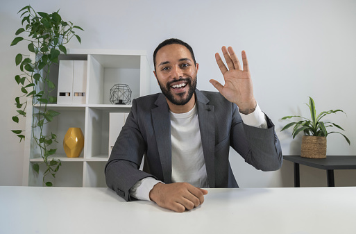 African american man in video call waving hand saying hello to coworkers. Smiling latino CEO looking at camera in business meeting. Business concept. Technology concept.