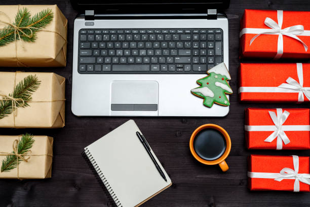 istock Open laptop computer, Christmas gift boxes, blank notebook and cup of coffee on dark wooden background, copy space. Top view, flat lay. Fir tree gingerbread cookie on keyboard 1341397065
