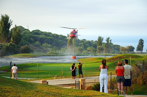 Bell 412 helicopter (registration N167EH) collecting water for fire fighting from a golf course lake, Cabopino Golf, Costa del Sol, Malaga Province, Andalucia, Spain, Western Europe.
