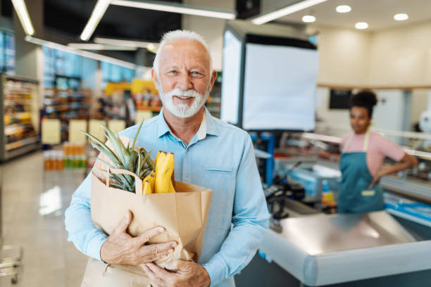Retired man buying groceries and smiling at camera People buying groceries in supermarket consumer confidence photos stock pictures, royalty-free photos & images