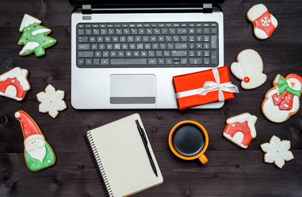 istock Laptop computer, blank notebook, Christmas present, cup of coffee and  gingerbread cookies on dark wood background 1341408883