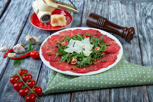 close-up carpaccio meat with arugula and slices of parmesan cheese.