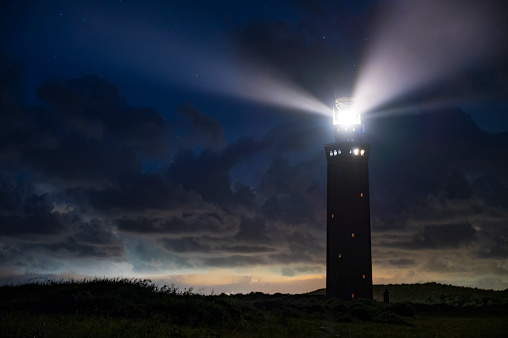 Lighthouse in the dunes with lightbeams at night. The Westhoofd lighthouse is situated on the Dutch North Sea coast near Ouddorp on Goeree-Overflakkee island in South-Holland.