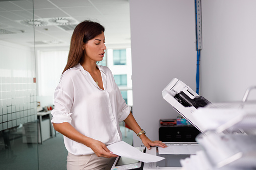 Woman working in the office standing by photocopier and copying documents