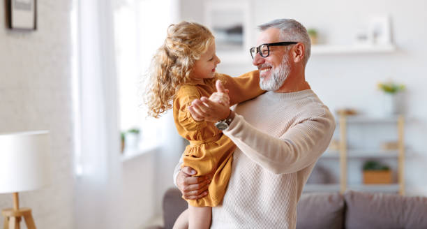 adorável menina criança e vovô positivo de mãos dadas enquanto dançavam juntos na sala de estar - grandchild - fotografias e filmes do acervo