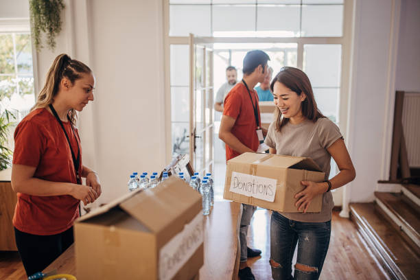 Woman donating boxes with food and clothes in donation center where volunteers are sorting packages stock photo