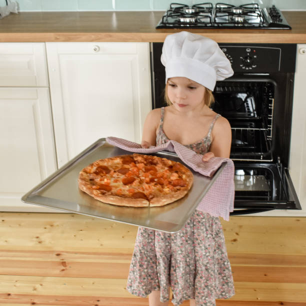女の子の子供はオーブンでピザを調理します - cheese making ストックフォトと画像