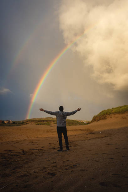 istock man with open arms admiring the rainbow 1341424380