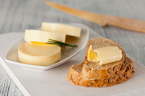 Piece of butter on bread with butter disks in plate next to it