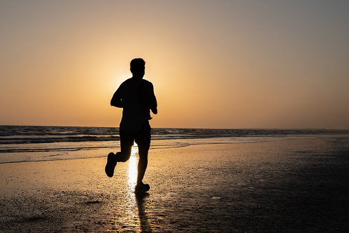 silhouette of a man running along the shore of the beach in an orange sunset