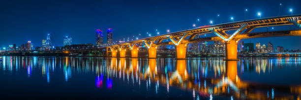 Bridge over river to neon night skyscraper cityscape panorama Seoul The spotlit span of the Cheongdam Bridge reflecting in the tranquil Han River to the glittering skyscrapers and highrise futuristic cityscape of Gangnam in the heart of Seoul, South Korea’s vibrant capital city. south korea photos stock pictures, royalty-free photos & images