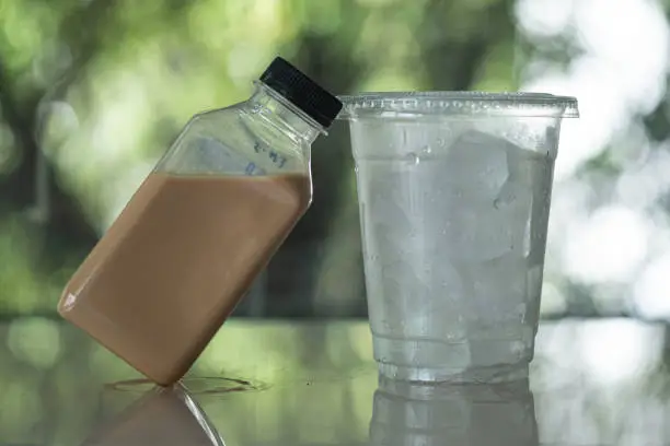 Photo of Ready to drink coffee in plastic bottle and ice cubes in glass. Quite popular during a pandemic