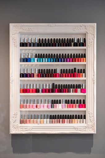 A picture frame shelf full of different colors of nail varnishes in a beauty salon.