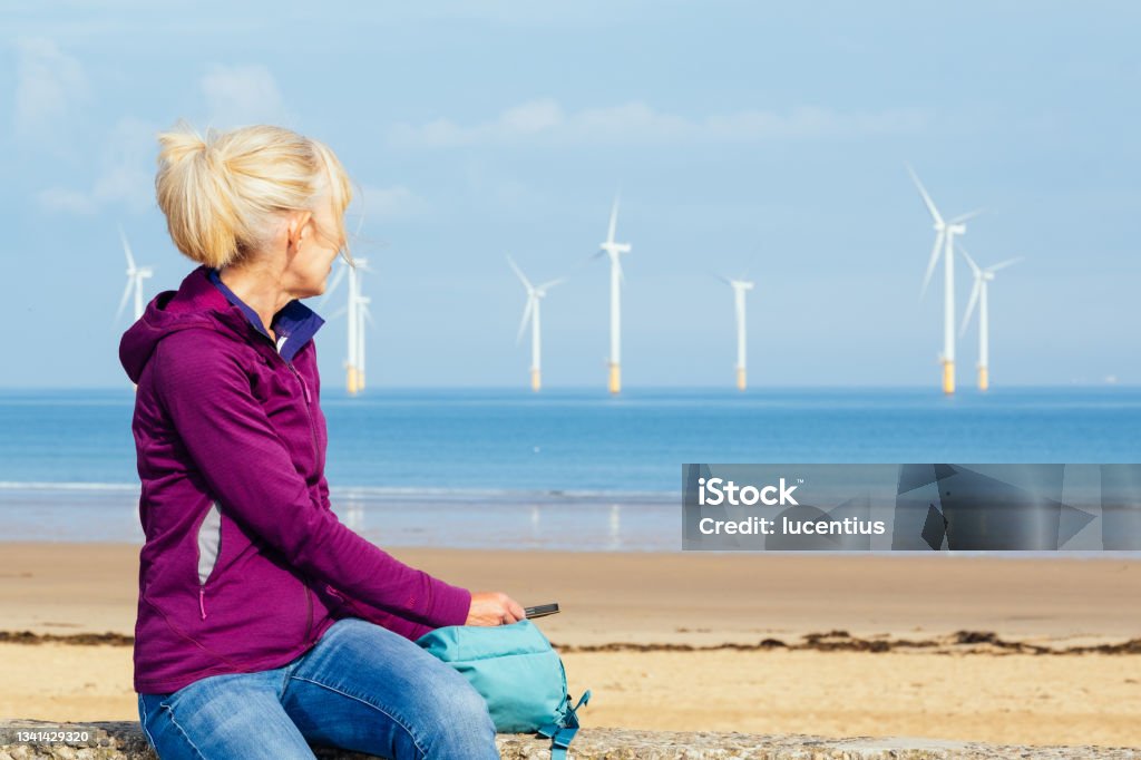 Offshore windfarm in the UK Woman observing an offshore windfarm at Redcar in the northeast of England. Offshore Platform Stock Photo