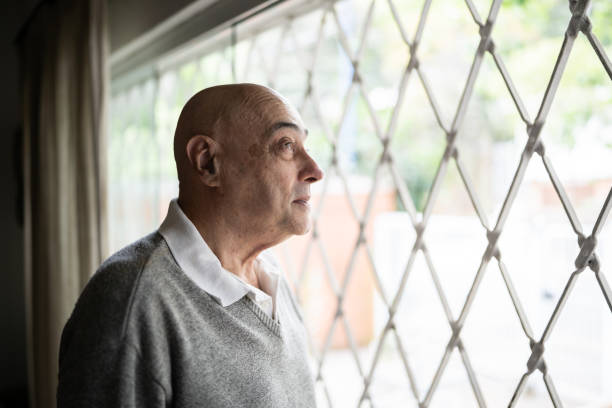 istock Senior man looking through window at home 1341429727