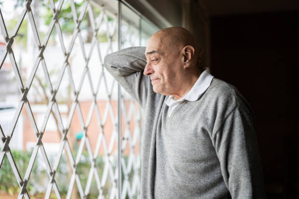 istock Worried senior man looking through window at home 1341429758