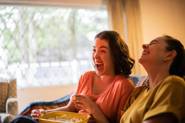 istock Happy sisters watching TV and eating popcorn at home 1341430852