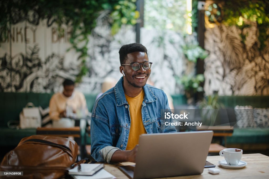 Young man on a video call in a cafe Young black man on a video conference call in a cafe. The concept of online tutoring. The concept of remotely working University Student Stock Photo