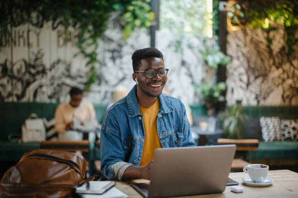 Young man on a video call in a cafe Young black man on a video conference call in a cafe. The concept of online tutoring. The concept of remotely working black man laptop stock pictures, royalty-free photos & images