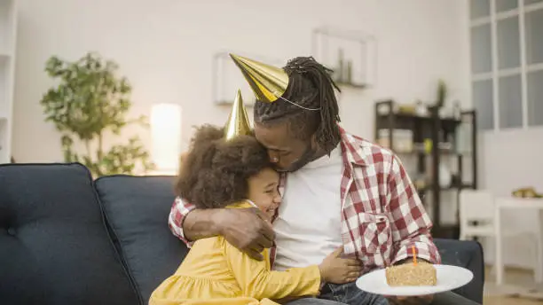 Young father wishing little daughter happy birthday with a cake, hugging and kissing