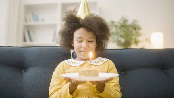 Cheerful afro-american girl blowing out candle on birthday cake, holiday celebration