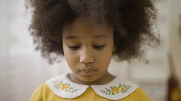 Sad black little girl with afro hair looking down, feeling lonely, upset, disappointed