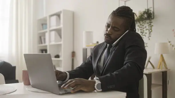 Black businessman talking on phone, typing on laptop, work, from home, freelance